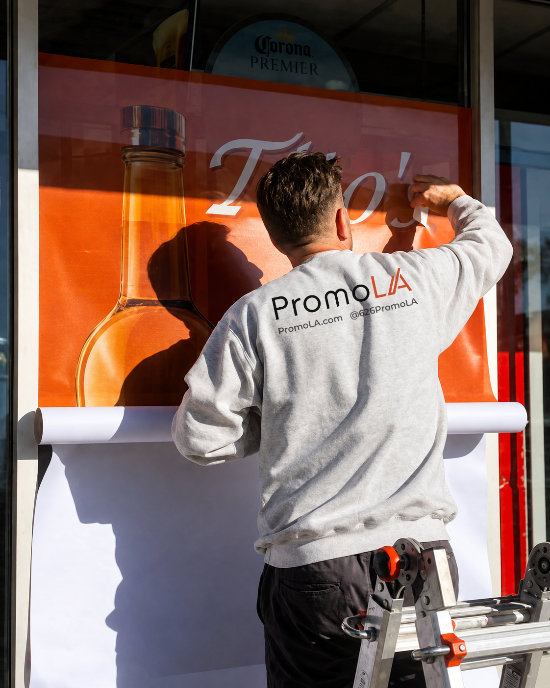 PromoLA installer in a branded sweatshirt applying a vinyl graphic to a storefront window